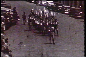 A troop of askaris (soldiers) marches along the street.